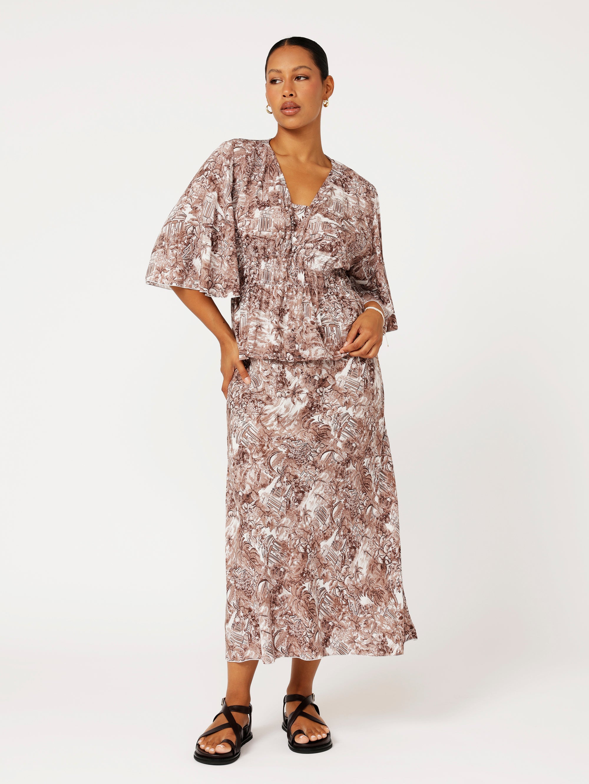 Front view of model wearing brown ruched top with fluted sleeves and matching print skirt