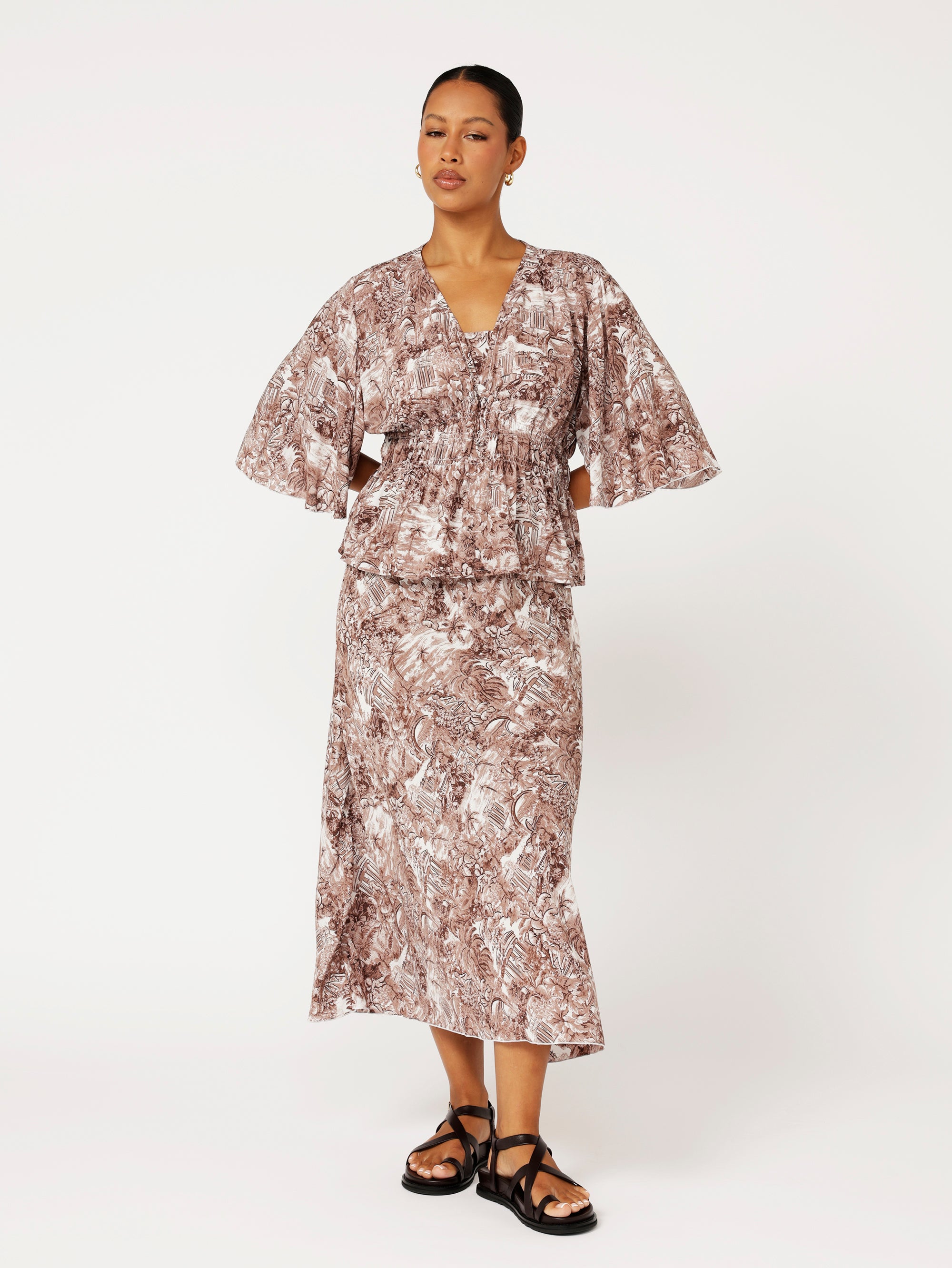 Front view of model wearing brown ruched top with fluted sleeves and matching print skirt
