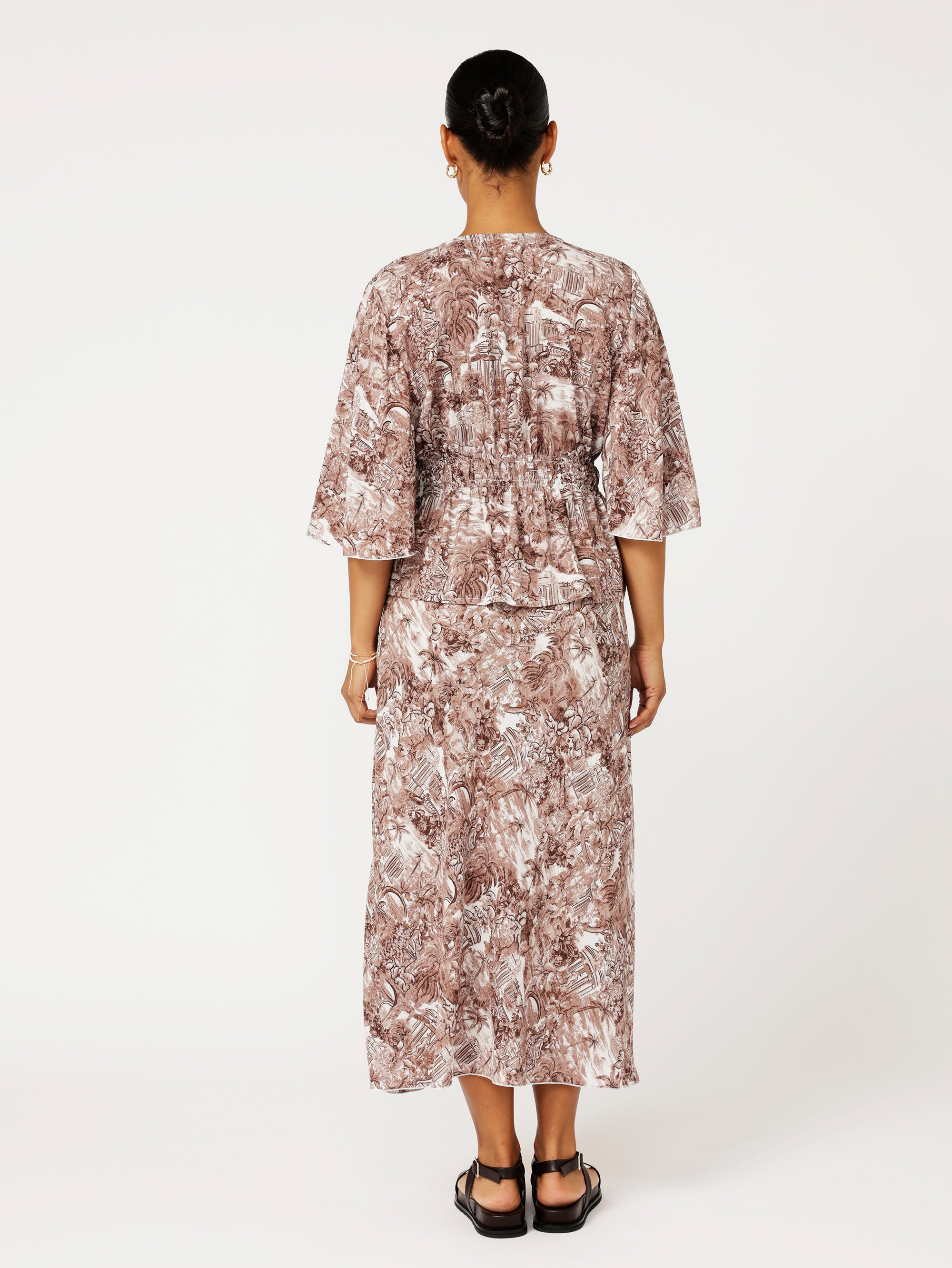back view of model wearing brown ruched top with fluted sleeves and matching print skirt