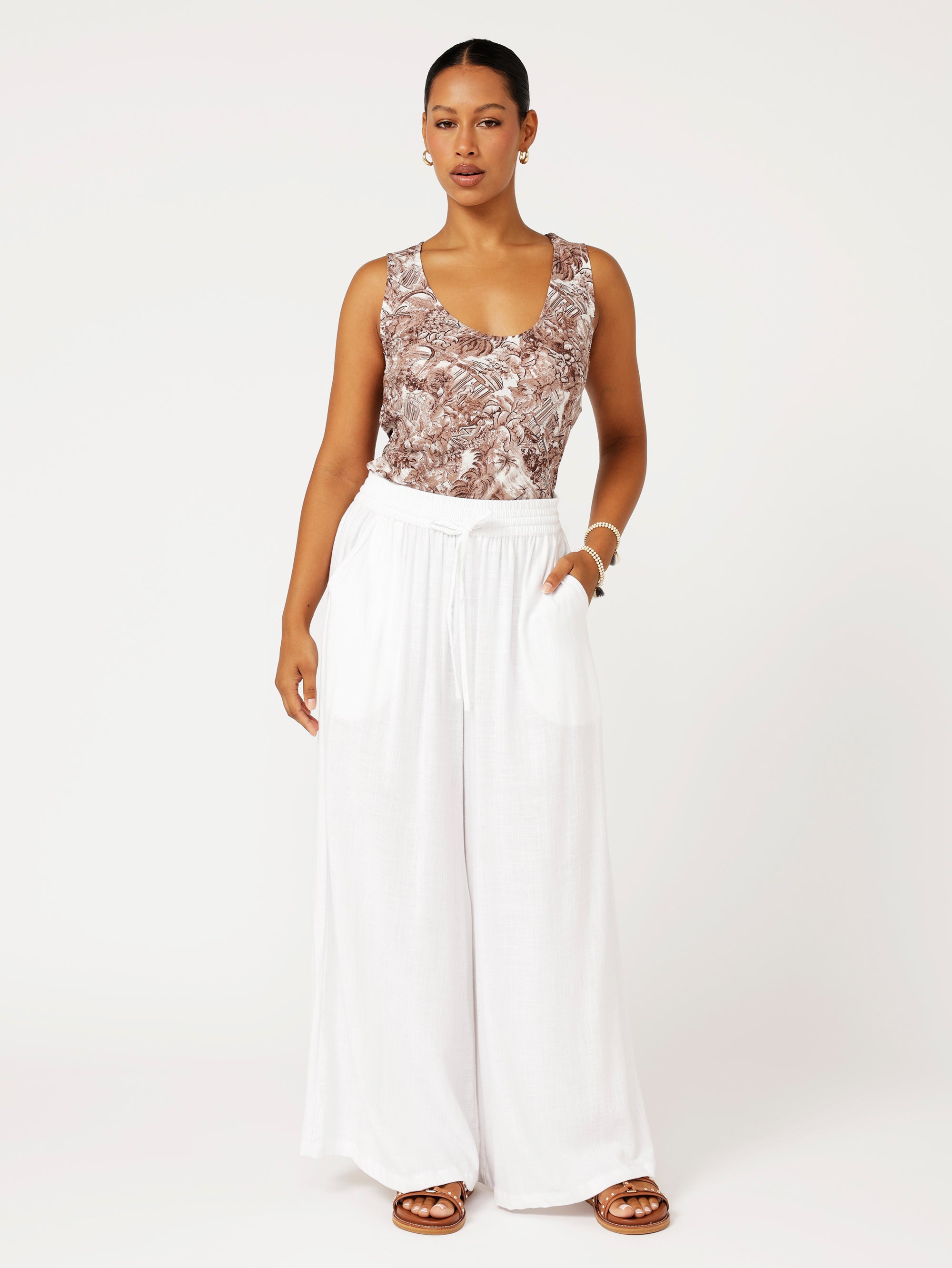 Front view of model wearing the Scoop Neck Top in brown Toile de Jouy rayon print paired with white wide-leg pants for a fresh resort look