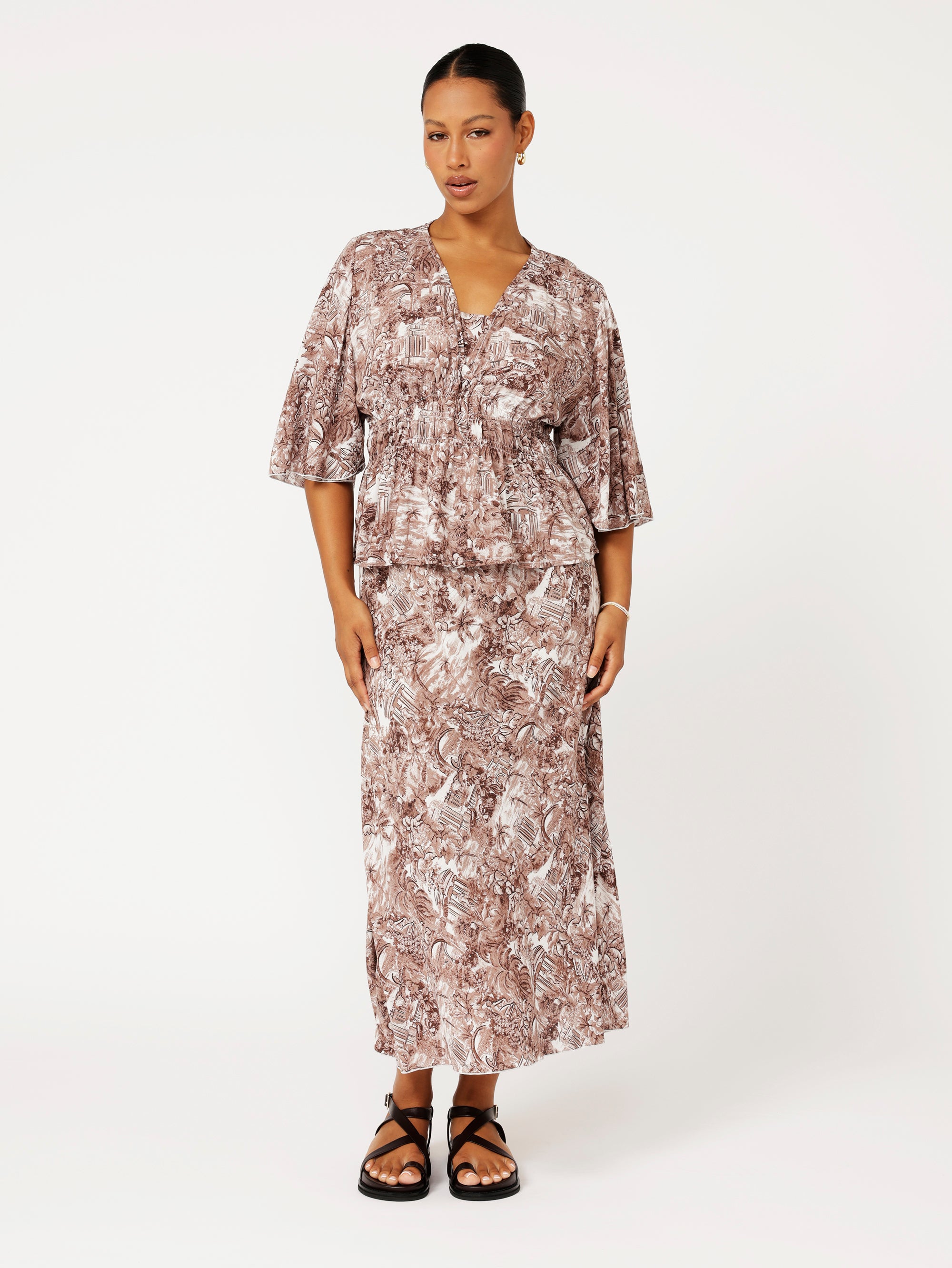 Front view of model wearing brown ruched top with fluted sleeves and matching print skirt.